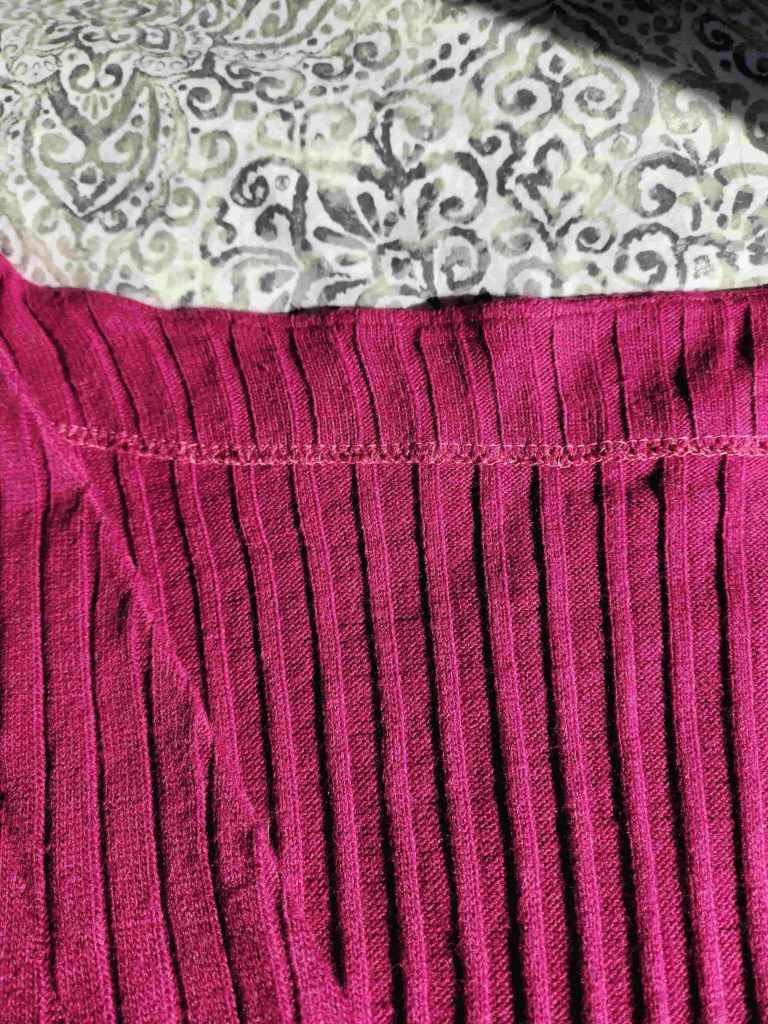 Ribbed sweater knit fabric stretch out at the neckline when attaching the facing. Serger finished edge.