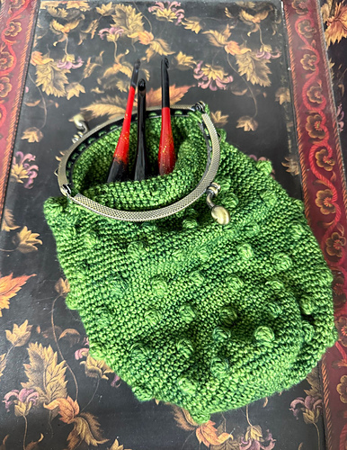 Crocheted pickle bag in green yarn with a clasp closure designed to be used to store crochet hooks. So cute!