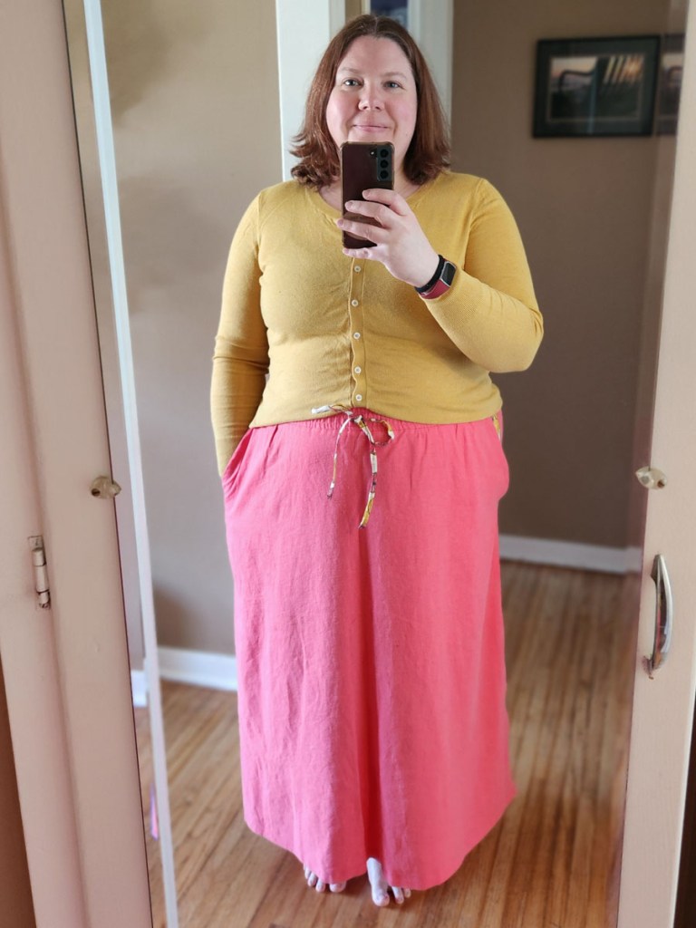 Love Notions Allegro Skirt made with coral linen fabric paired with a yellow sweater on a plus-sized woman.