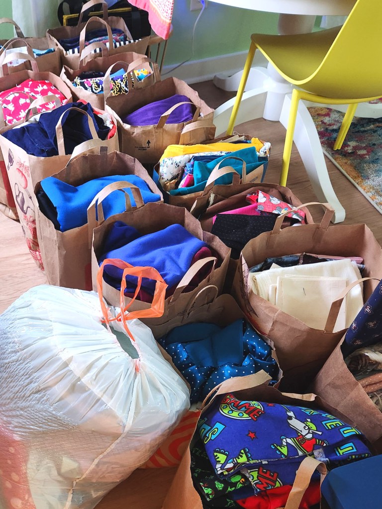14 plus bags stuffed with different colors, types, and amounts of fabric to gift back to the community.